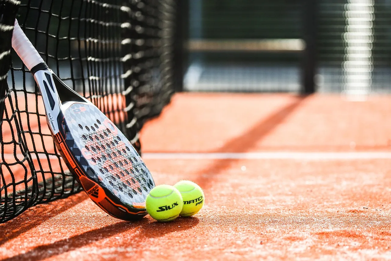Une raquette de padel et deux balles au pied du filet